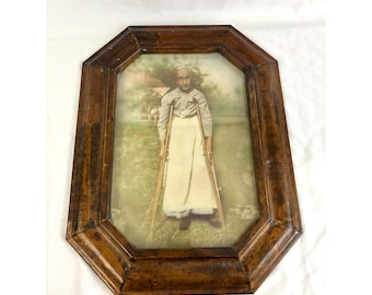 Fotografía antigua enmarcada de una mujer con muletas, marco octogonal de madera, retrato vintage.