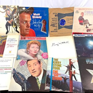 May include: A collection of vintage vinyl records with album covers featuring musicians, portraits, and graphic designs. Titles include "More Brass," "Woody Woodbury," and "Starburst." The records are in various colors and designs.