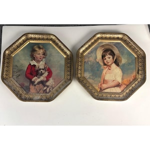 May include: Two vintage decorative trays. One tray features a portrait of a child in a red jacket holding a small dog. The other tray shows a portrait of a child in a white dress and a hat. Both trays have a gold octagonal frame.