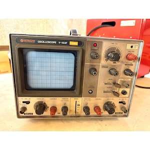 Puede incluir: Osciloscopio Hitachi V-152F vintage, 15 MHz. El dispositivo tiene una carcasa metálica negra y gris, una pantalla con una cuadrícula y numerosas perillas y diales. El texto "HITACHI OSCILLOSCOPE V-152F" es visible.