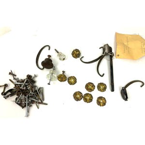 May include: Assortment of vintage hardware including drawer pulls, cabinet knobs, hooks, and screws. The hardware is made of metal and has a variety of finishes, including brass, nickel, and chrome.