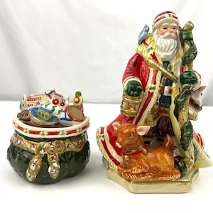 Peut inclure: Une figurine en céramique de Père Noël tenant une lanterne et un sac de jouets. La figurine est décorée de couleurs rouge, blanc et vert. Le sac de jouets est rempli d'une variété de jouets, dont un bateau jouet, un tambour jouet et un train jouet.