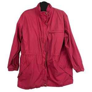 Puede incluir: Una chaqueta rosa de manga larga con cierre de cremallera y cintura con cordón. La chaqueta tiene un pequeño logotipo en el pecho izquierdo que dice "Columbia".