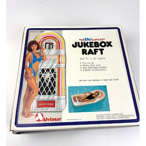 Puede incluir: Flotador hinchable de máquina de discos en caja, aproximadamente 191 cm x 81 cm, con diseño retro. Presenta a una mujer en traje de baño azul y el texto "JUKEBOX RAFT". Incluye portavasos y construcción con vigas en I. Para mayores de 13 años.