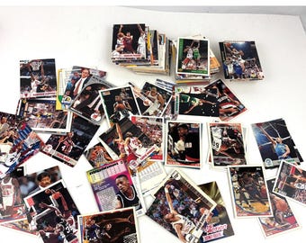 Könnte beinhalten: Eine Sammlung von Basketball-Sammelkarten im Vintage-Stil mit verschiedenen Spielern in Actionposen. Die Karten zeigen leuchtende Farben und Actionaufnahmen, die Spieler in der Luft und während des Spiels zeigen. Die Karten sind auf einer weißen Oberfläche verstreut.