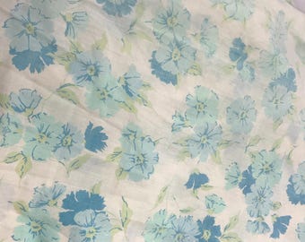 Puede incluir: Tela blanca con un patrón floral azul. Las flores son de un azul claro con un centro azul más oscuro. La tela es suave y tiene un brillo sutil.