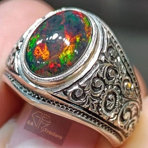 May include: A silver ring with an ornate design and a large oval-shaped opal gemstone. The opal is a vibrant mix of green, red, and black.