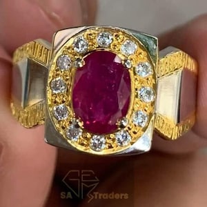 May include: A gold and silver ring featuring a large oval ruby surrounded by smaller diamonds. The ring has a textured band.