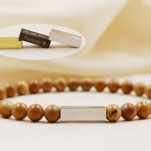 May include: A bracelet featuring brown, spherical beads and a silver rectangular bar. The image also shows three small rectangular bars, one gold, one silver, and one black with the inscription "06.08.2023 Forever".