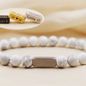 May include: White howlite bead bracelet with a silver bar charm. The charm has an engraved inscription that reads "Create Love U".