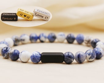 May include: A blue and white beaded bracelet with a black rectangular charm. The charm has the words "Create Love U" engraved on it.
