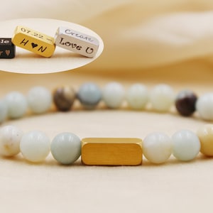 May include: A light green, white and beige beaded bracelet with a gold bar charm. The bracelet has a personalised charm with the text "Create Love U".