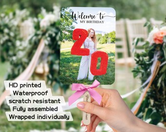 May include: A rectangular handheld sign featuring a photo of a person in a white outfit with the red number 20 overlaid and the text Welcome to MY BIRTHDAY. The sign has a wooden handle with a pink satin ribbon bow and is labeled as HD printed.