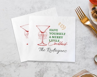May include: Two white square paper napkins featuring a red martini glass illustration with a bow, a gold star, and the green and red text "HAVE YOURSELF A MERRY LITTLE COCKTAIL" followed by the black script name "The Rodriguez" printed below.