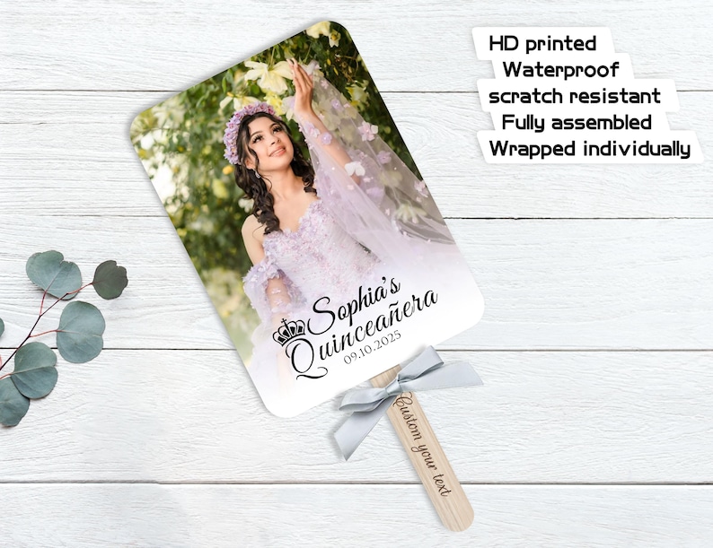 May include: A personalized fan featuring a photo of a woman in a lavender dress, with the text "Sophia's Quincea&ntilde;era 09.10.2025." The fan has a wooden handle with a gray ribbon and the text "Custom your text."