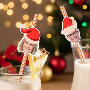 Könnte beinhalten: Zwei Gläser eines cremigen Getränks mit festlichen Strohhalmen. Jeder Strohhalm hat einen Weihnachtsmütze mit dem Gesicht einer Person. Die Strohhalme sind orange und weiß gestreift. Der Hintergrund hat Weihnachtsdekorationen und Bokeh-Lichter.