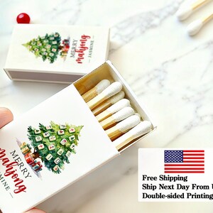 May include: Matchbox with a Christmas tree design and the text "Merry Mahjong - Jasmine" in red script. The matchbox contains wooden matches with white tips. The design includes gift boxes at the base of the tree.