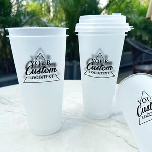 Puede incluir: Tres vasos de plástico blanco con acabado mate. Cada vaso tiene un triángulo negro con el texto "YOUR Custom LOGO/TEXT" impreso en él.