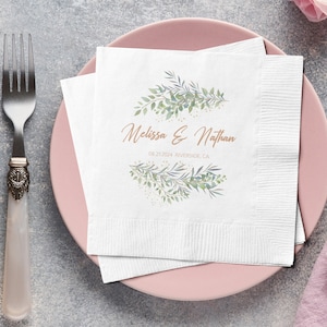 Pode incluir: Guardanapo de papel branco com um design floral verde e dourado e o texto "Melissa & Nathan 08.23.2014 Riverside, CA". O guardanapo está em um prato rosa com um garfo e uma faca de prata.