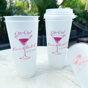 Op de afbeelding: Drie witte plastic bekers met een roze martini-glasontwerp en de tekst "Cin-Cin! Kevin & Rachel" en de datum van het evenement.