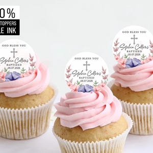 May include: Three pink frosted cupcakes with edible toppers. Each topper is a circle with a white background and a floral design. The text on the toppers reads "God Bless You", "+", "Sophia Collins", "Baptized", and "05.07.2026".