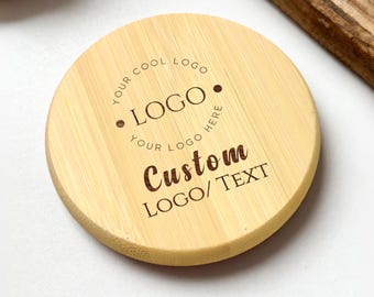Puede incluir: Un posavasos redondo de bambú de color claro con texto grabado. El texto incluye "YOUR COOL LOGO HERE" alrededor de la palabra "LOGO" y "Custom LOGO/TEXT" debajo. El posavasos tiene un patrón de vetas de madera natural.
