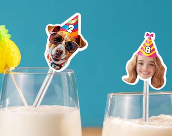 Puede incluir: Dos agitadores de cóctel con recortes decorativos. Uno presenta un perro con gafas de sol y un gorro de fiesta con el número 2. El otro muestra a una niña con un gorro de fiesta con el número 8. Ambos están en vasos con una bebida blanca.