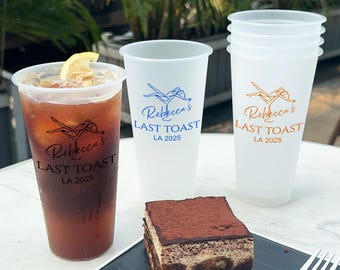 Puede incluir: Tres vasos de plástico escarchados con el texto "Rebecca's Last Toast LA 2025" impreso en ellos. Los vasos están llenos de un líquido transparente. Una rodaja de limón está en uno de los vasos. Un trozo de pastel de chocolate está en primer plano.