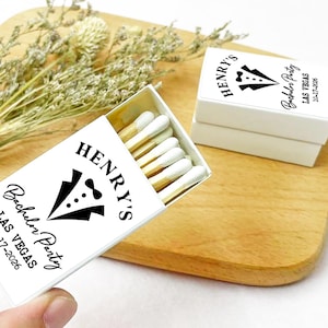 May include: White matchbox with black text and a tuxedo graphic. The text reads "Henry's Bachelor Party Las Vegas 10-17-2026".