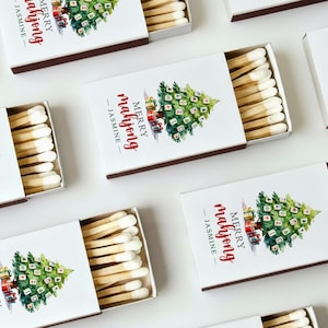 May include: White matchboxes with a Christmas tree design and the text "MERRY mahjong - JASMINE". The matches are visible inside the open boxes. The boxes have a brown border.