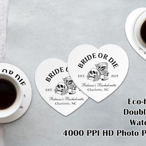 Könnte beinhalten: Herzförmige weiße Untersetzer mit schwarzem Text und Totenkopf-Grafiken, die "BRIDE OR DIE" und "Rebecca's Bachelorette, Charlotte, NC" zeigen. Zwei Tassen Kaffee stehen auf Untersetzern. Der Text "Eco-friendly Double-sided Waterproof 4000 PPI HD Photo Printing" ist ebenfalls sichtbar.