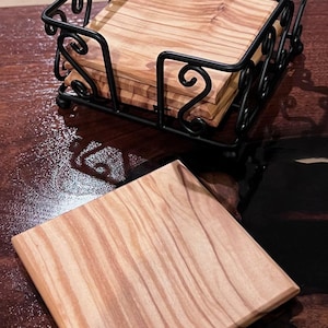 May include: A set of six wooden coasters with a natural wood grain pattern, stacked in a black metal holder with a decorative scroll design.