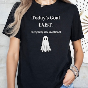 May include: A black short-sleeved t-shirt featuring white text that reads Today's Goal EXIST. Everything else is optional. Below the text is a simple white graphic of a ghost with two black oval eyes, centered on the front of the garment.