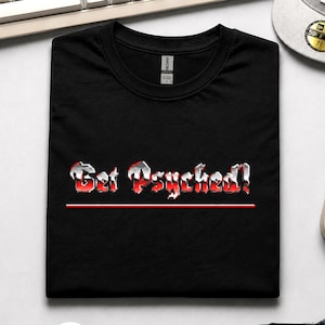 May include: A black short-sleeved t-shirt featuring the text "Get Psyched!" in a metallic, chrome-like font with red accents. The graphic includes a thin red horizontal line underneath the text. The shirt has a crew neckline and a Gildan brand label.