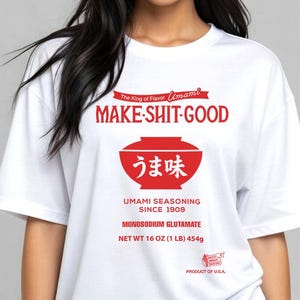 May include: White t-shirt with a red graphic that reads "MAKE-SHIT-GOOD" above a bowl design with Japanese text. Below the bowl, it says "UMAMI SEASONING SINCE 1909" and "MONOSODIUM GLUTAMATE". The shirt is labeled "NET WT 16 OZ (1 LB) 454g" and "PRODUCT OF U.S.A."