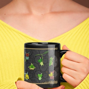 Puede incluir: Taza de cer&aacute;mica negra con un dise&ntilde;o de personajes de dibujos animados verdes y amarillos sobre un fondo blanco y negro. Los personajes est&aacute;n rodeados de c&iacute;rculos conc&eacute;ntricos. La taza tiene un asa blanca.