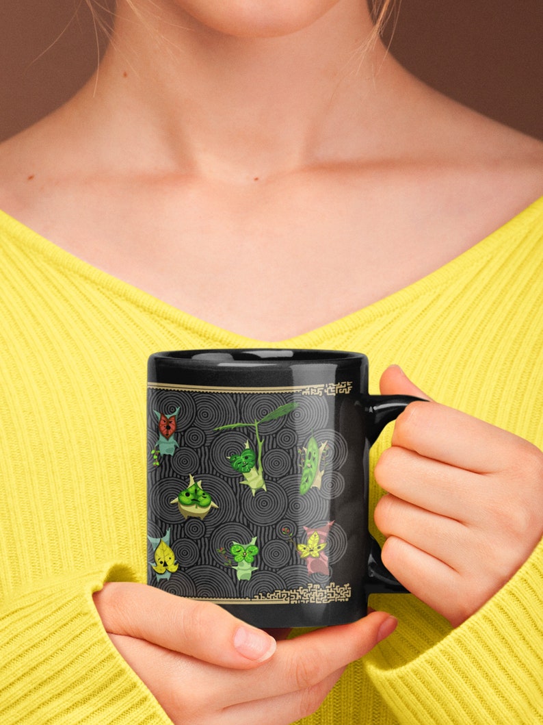 Puede incluir: Taza de cer&aacute;mica negra con un dise&ntilde;o de personajes de dibujos animados verdes y amarillos sobre un fondo blanco y negro. Los personajes est&aacute;n rodeados de c&iacute;rculos conc&eacute;ntricos. La taza tiene un asa blanca.