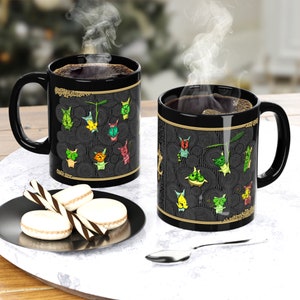 Puede incluir: Dos tazas de caf&eacute; negras con un borde dorado y un dise&ntilde;o negro y dorado con criaturas de dibujos animados de colores. Las tazas est&aacute;n llenas de caf&eacute; y sale vapor de la parte superior de las tazas.
