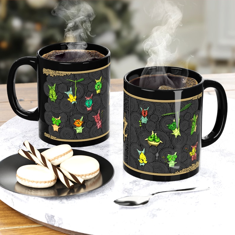 Puede incluir: Dos tazas de caf&eacute; negras con un borde dorado y un dise&ntilde;o negro y dorado con criaturas de dibujos animados de colores. Las tazas est&aacute;n llenas de caf&eacute; y sale vapor de la parte superior de las tazas.