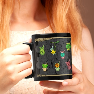 Puede incluir: Una taza de cer&aacute;mica negra con un borde dorado y un dise&ntilde;o de personajes de dibujos animados verdes, amarillos y azules sobre un fondo negro y dorado.