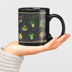 Puede incluir: Taza de cer&aacute;mica negra con un dise&ntilde;o de criaturas verdes, amarillas y rojas sobre un fondo negro y dorado. Las criaturas est&aacute;n rodeadas de c&iacute;rculos conc&eacute;ntricos.