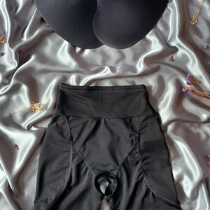 May include: Black undergarment with a high waist and a cutout in the back. The undergarment has a smooth, seamless design and is made of a stretchy fabric.