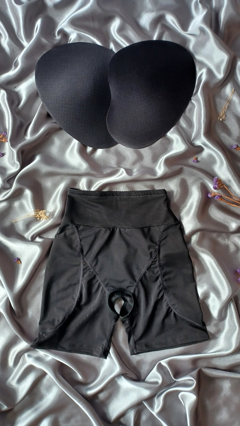 May include: Black undergarment with a high waist and a cutout in the back. The undergarment has a smooth, seamless design and is made of a stretchy fabric.