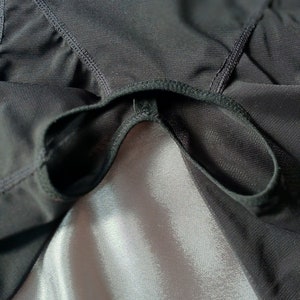 May include: Black mesh fabric with a black elastic band sewn around the edge. The fabric is draped over a white satin surface.