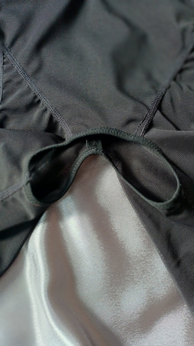 May include: Black mesh fabric with a black elastic band sewn around the edge. The fabric is draped over a white satin surface.