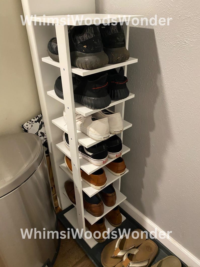 May include: White shoe rack with six shelves, holding a variety of shoes, including sneakers, sandals, and dress shoes. The rack is against a white wall and has the text "Whims Woods Wonder" on the top and bottom.