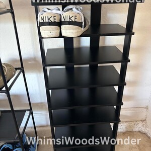 May include: Black shoe rack with six shelves. The top shelf has two white sneakers with black Nike logos. The shoe rack is labeled "Whims Woods Wonder".
