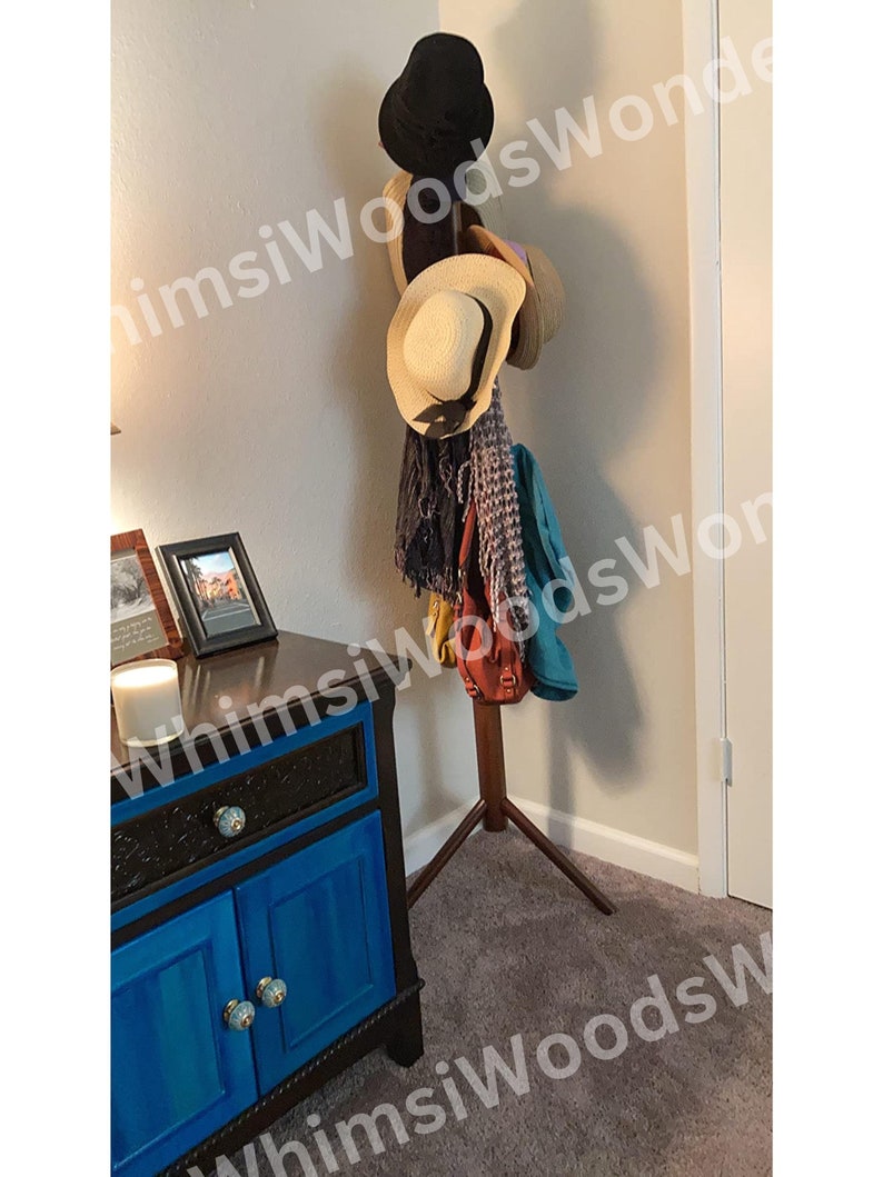 May include: A wooden hat rack with a dark finish holds several hats and scarves. The hats include a black fedora and several straw hats. A blue cabinet with ornate details and a candle are in the foreground.