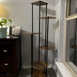 May include: A five-tier wooden shelf unit with black metal supports. The shelves are a rustic brown color and the metal supports are black. The shelf unit is standing on a carpeted floor.