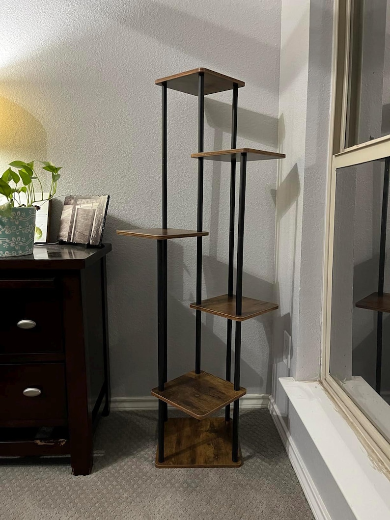 May include: A five-tier wooden shelf unit with black metal supports. The shelves are a rustic brown color and the metal supports are black. The shelf unit is standing on a carpeted floor.